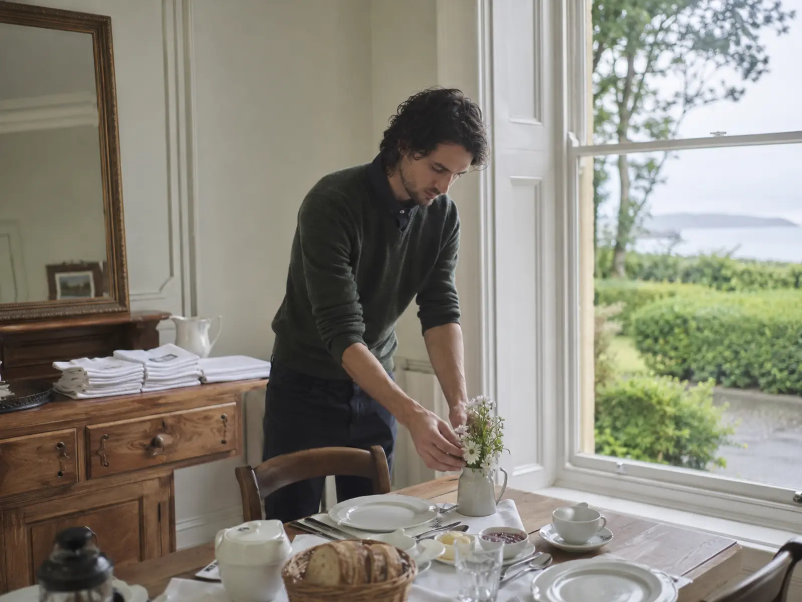 A guesthouse owner setting a table in a bright room near the coast