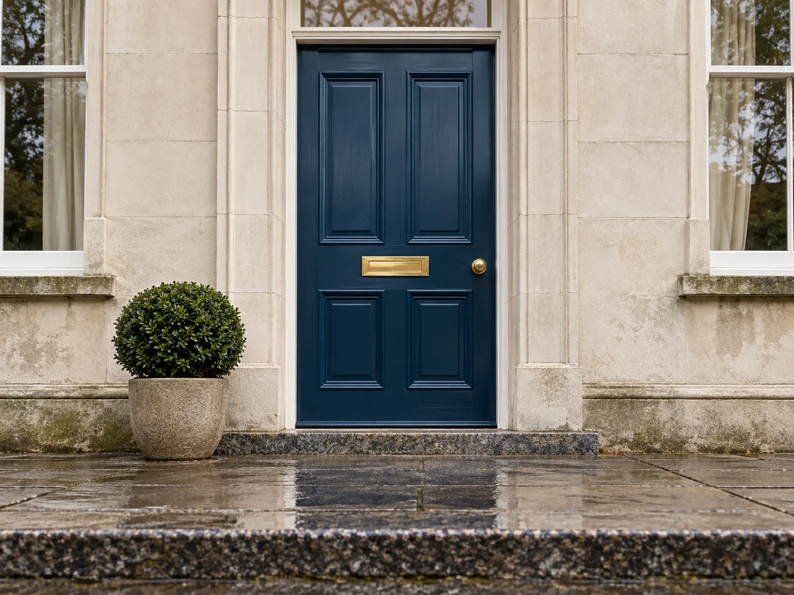 A deep blue townhouse front door with a brass letterbox on a wet granite step