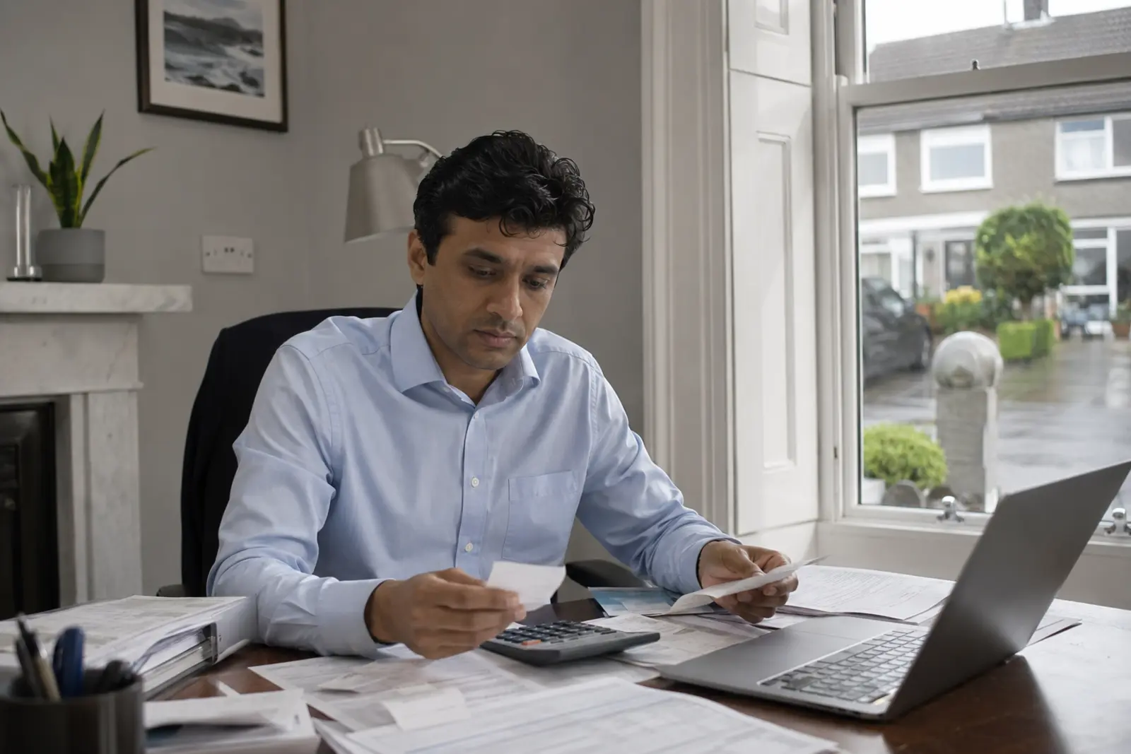 An accountant working through receipts with a calculator and laptop