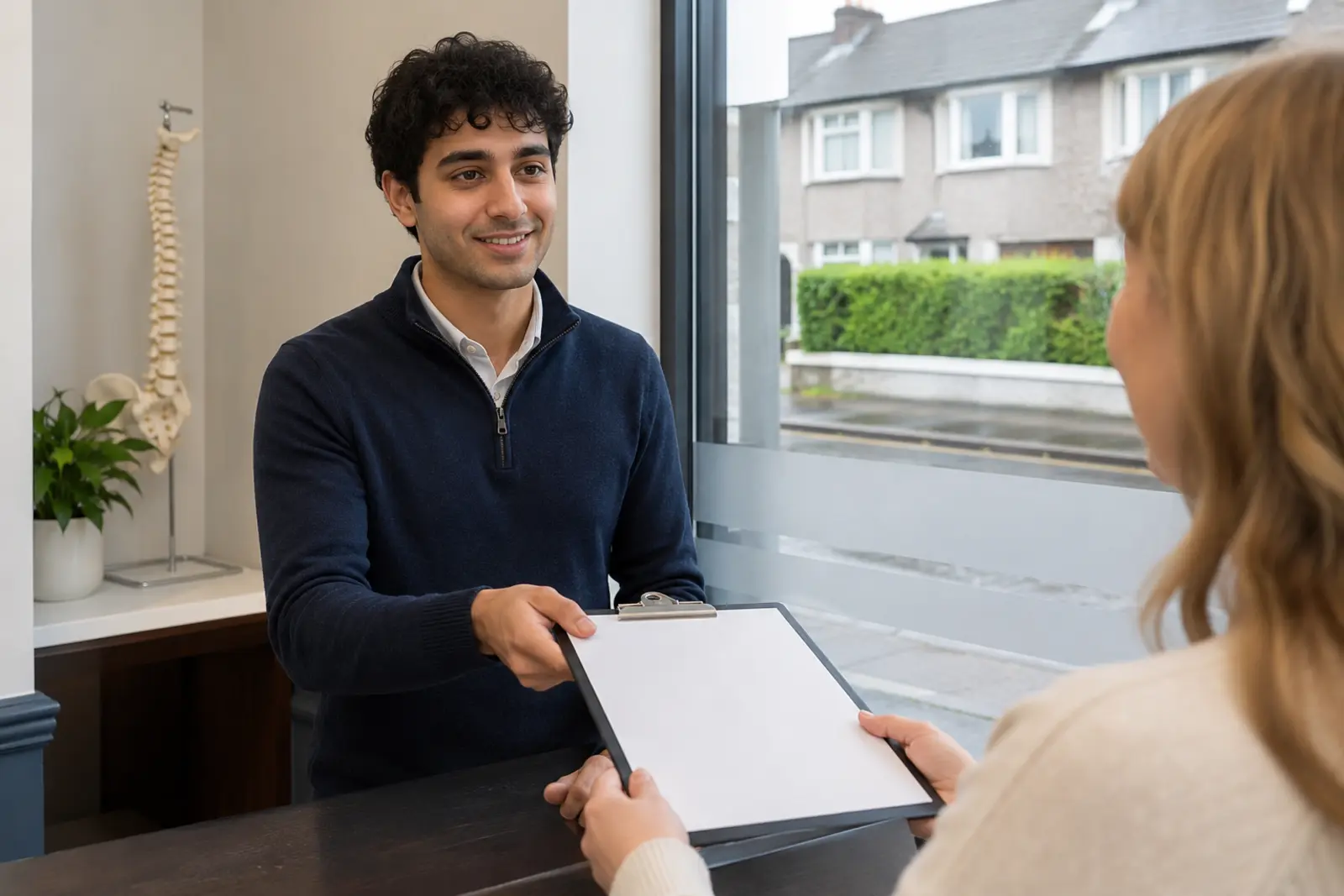 A chiropractor handing a new-patient form to a client at the clinic reception desk