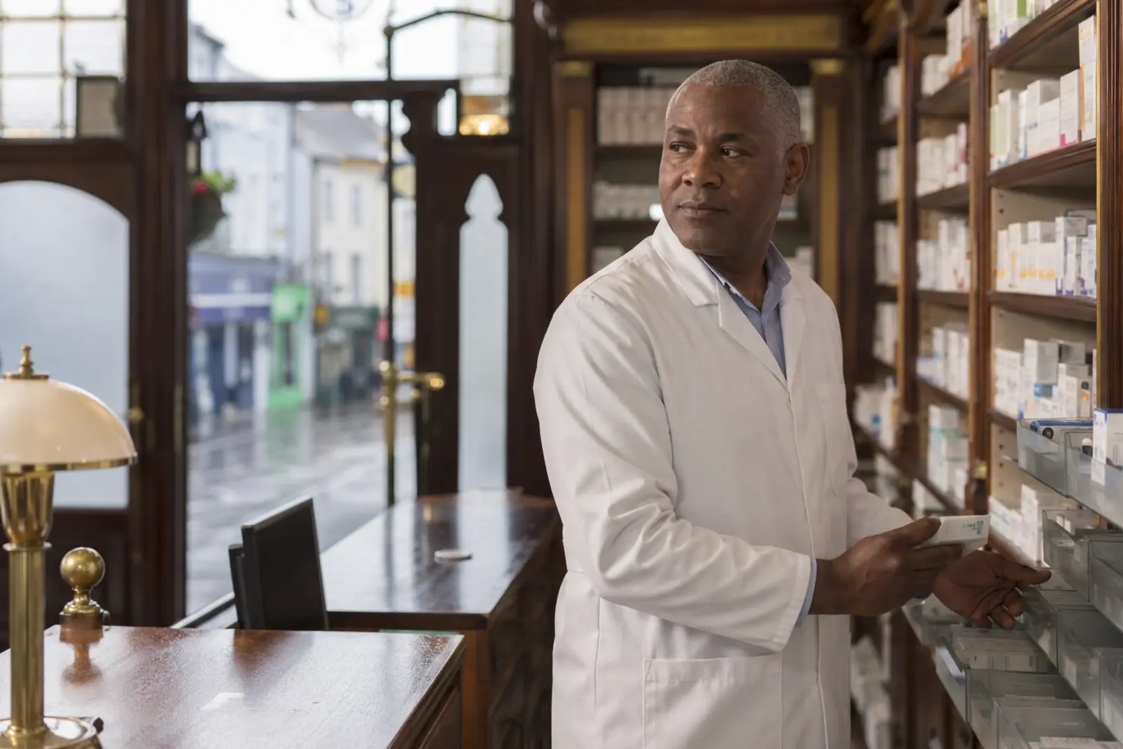 A pharmacist checking stock on the shelves in a traditional community pharmacy