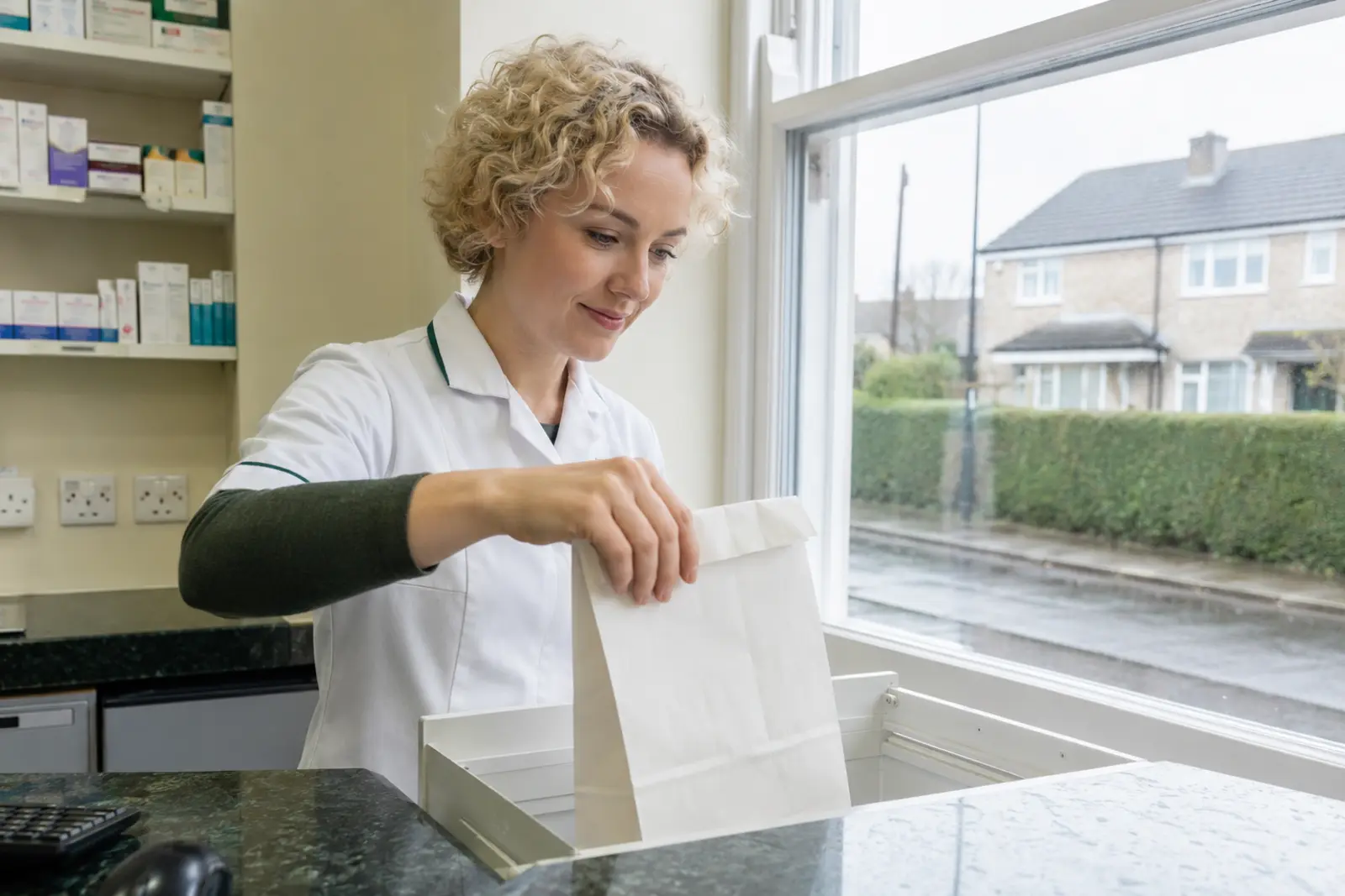 A pharmacy assistant filling a prescription bag at the dispensary counter