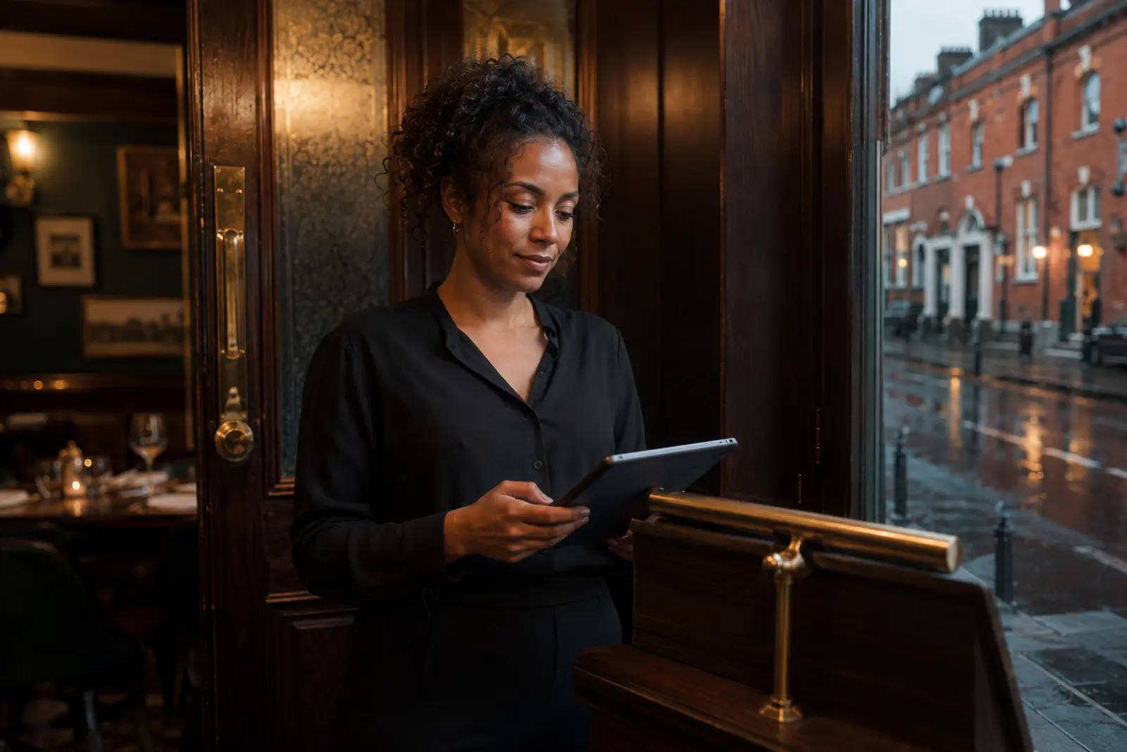 A host checking reservations on a tablet at the door of a restaurant