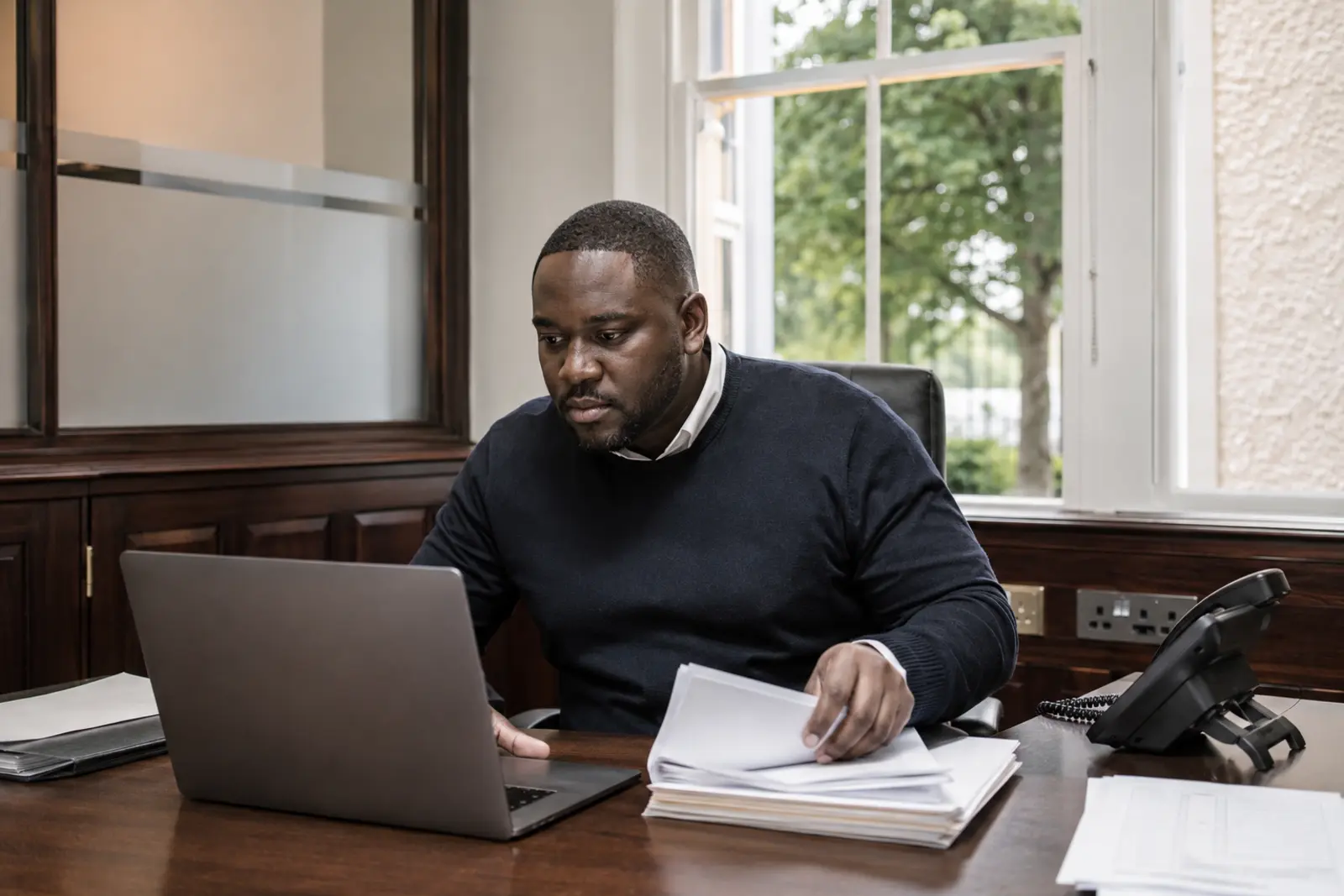 A solicitor at a laptop sorting through paperwork in a panelled office